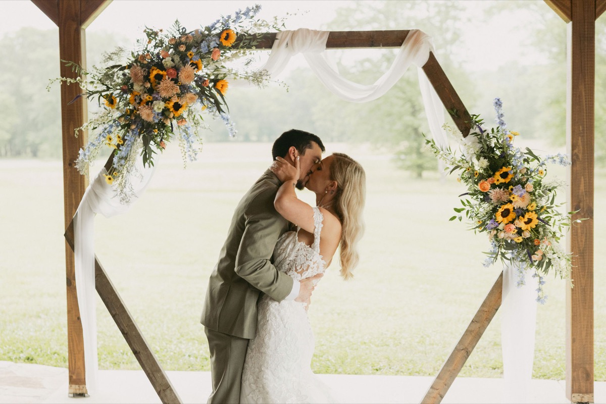 Brianna & Michael share a first kiss under a sunflower-draped hexagonal arbor in Covey Creek's open patio pavilion.