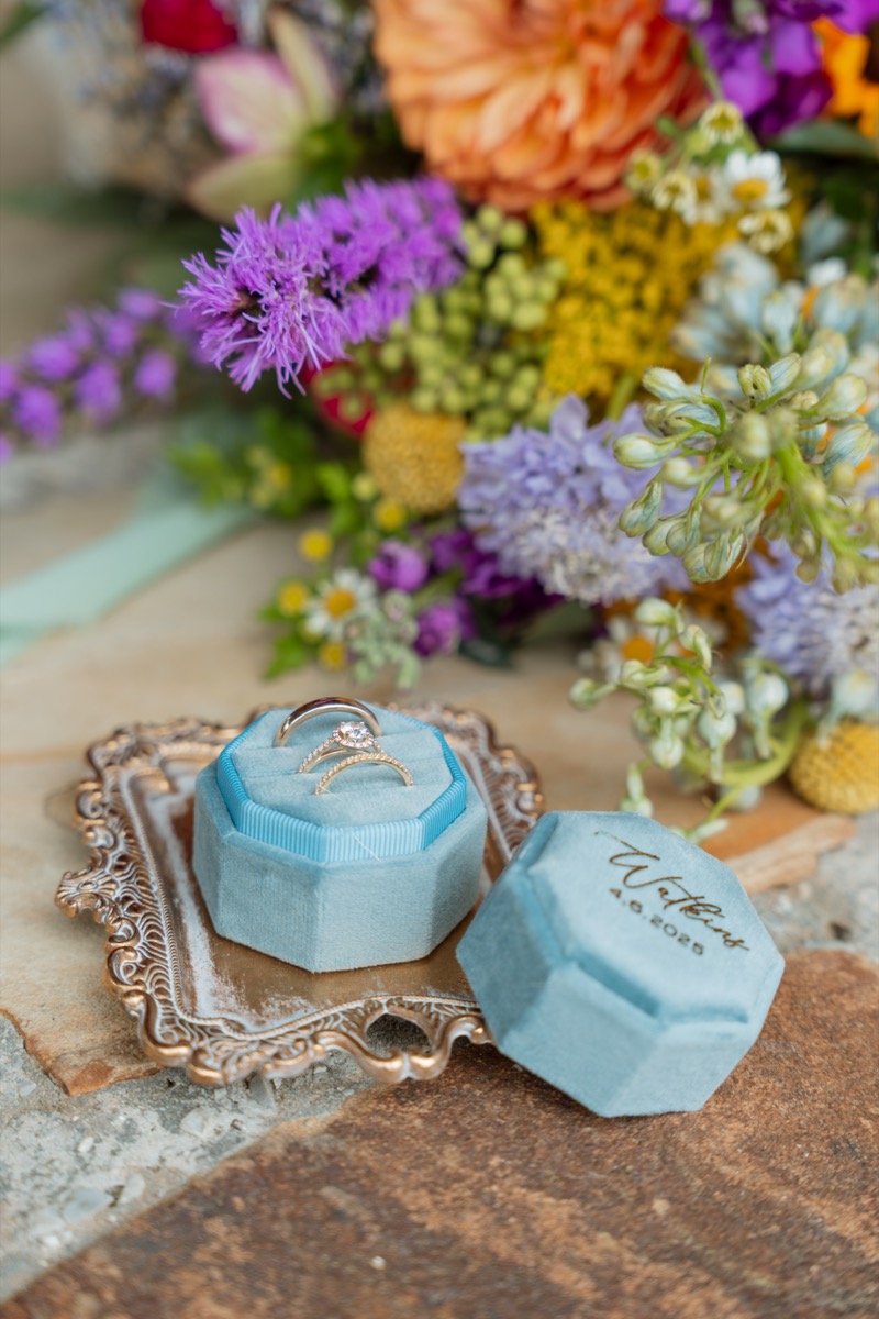 Caitlin & Daniel rings rest in a blue Watkins velvet box beside their colorful bouquet at Covey Creek