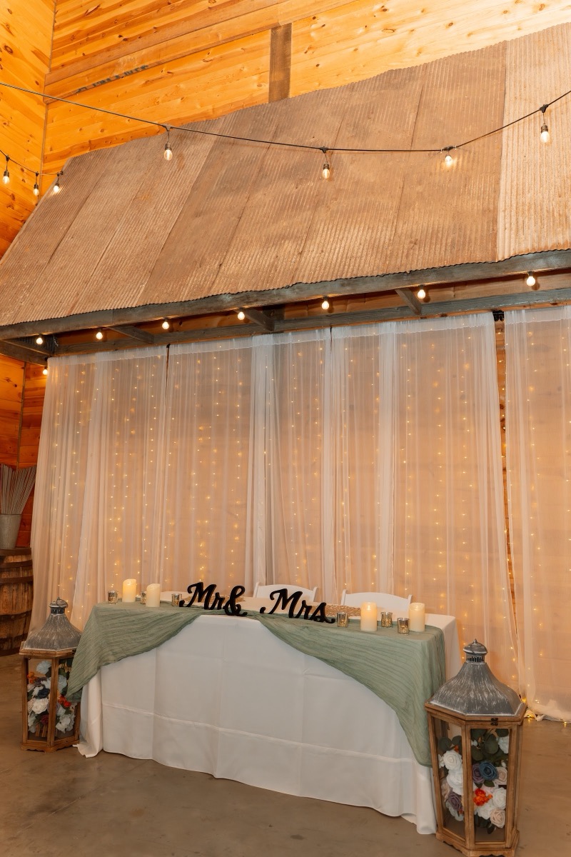 Caitlin & Daniel sweetheart table with Mr. & Mrs. sign, candles, and sheer lit backdrop at Covey Creek