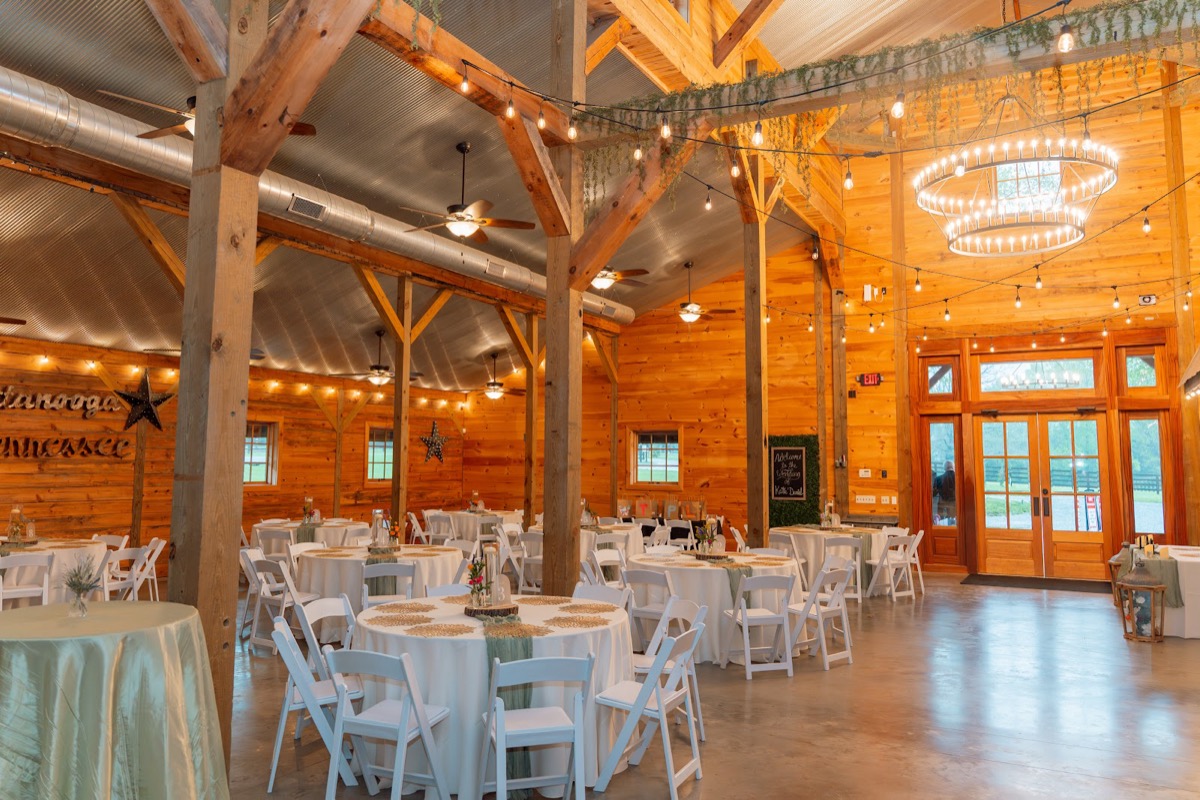 Caitlin & Daniel reception hall with round tables, sage runners, and string lights in the barn at Covey Creek