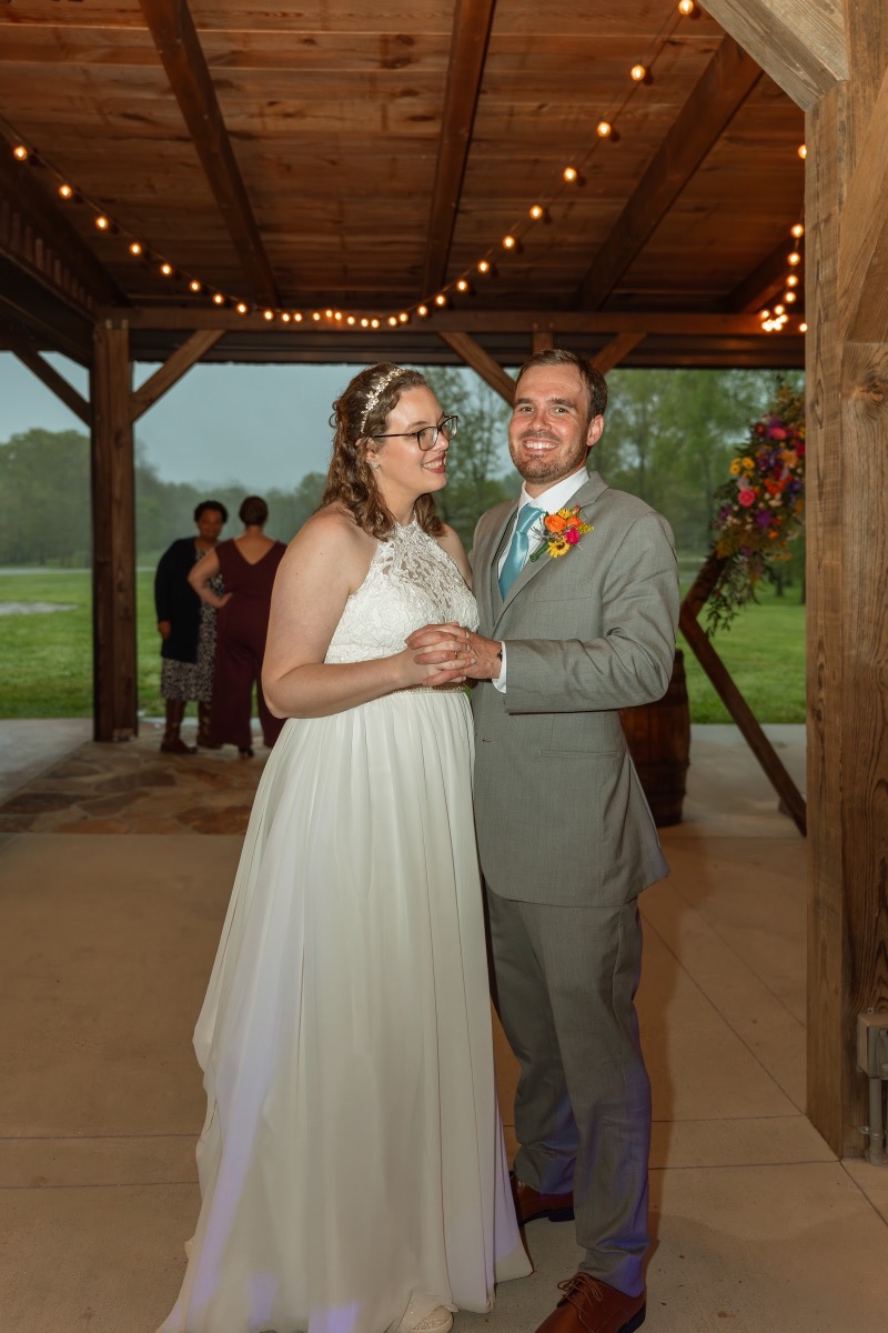 Caitlin & Daniel smile hand-in-hand under string lights at the Pond pavilion after ceremony at Covey Creek