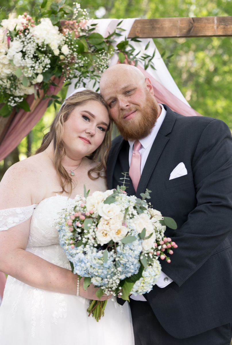 Carly & Lucas lean forehead to forehead under a floral arbor at their Tunnel of Love ceremony at Covey Creek