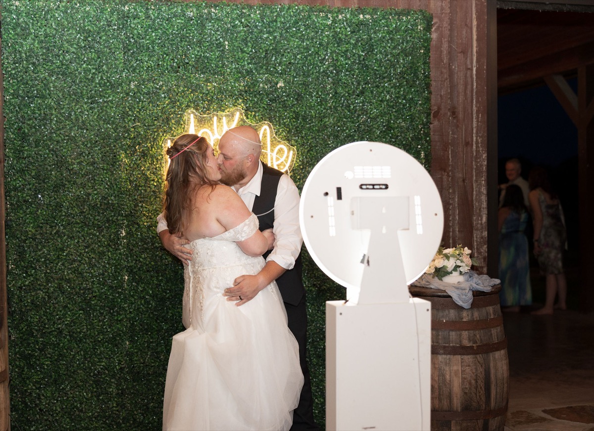 Carly & Lucas kiss beside a neon hedge wall and photo booth at their Covey Creek indoor reception
