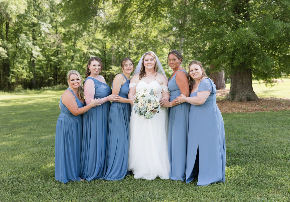 Carly poses with five bridesmaids in dusty blue dresses on the lawn at Covey Creek, Carly & Lucas wedding