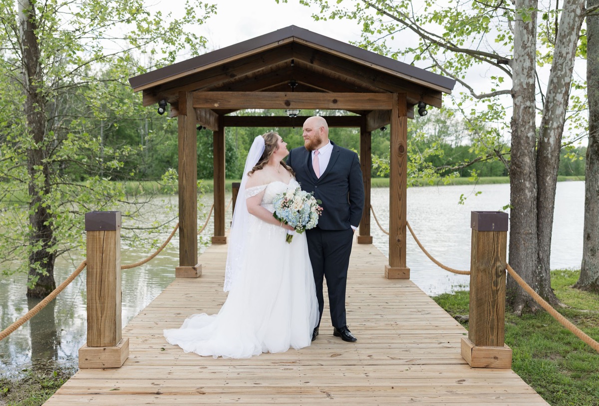 Carly & Lucas stand face-to-face on the wooden Pond pavilion dock at Covey Creek with rope railings