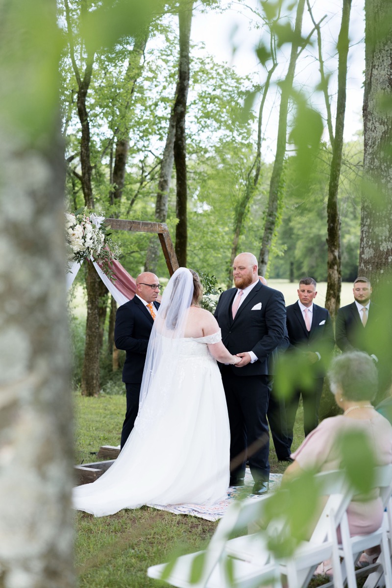 Carly & Lucas hold hands under a floral wooden arbor at their Tunnel of Love ceremony at Covey Creek