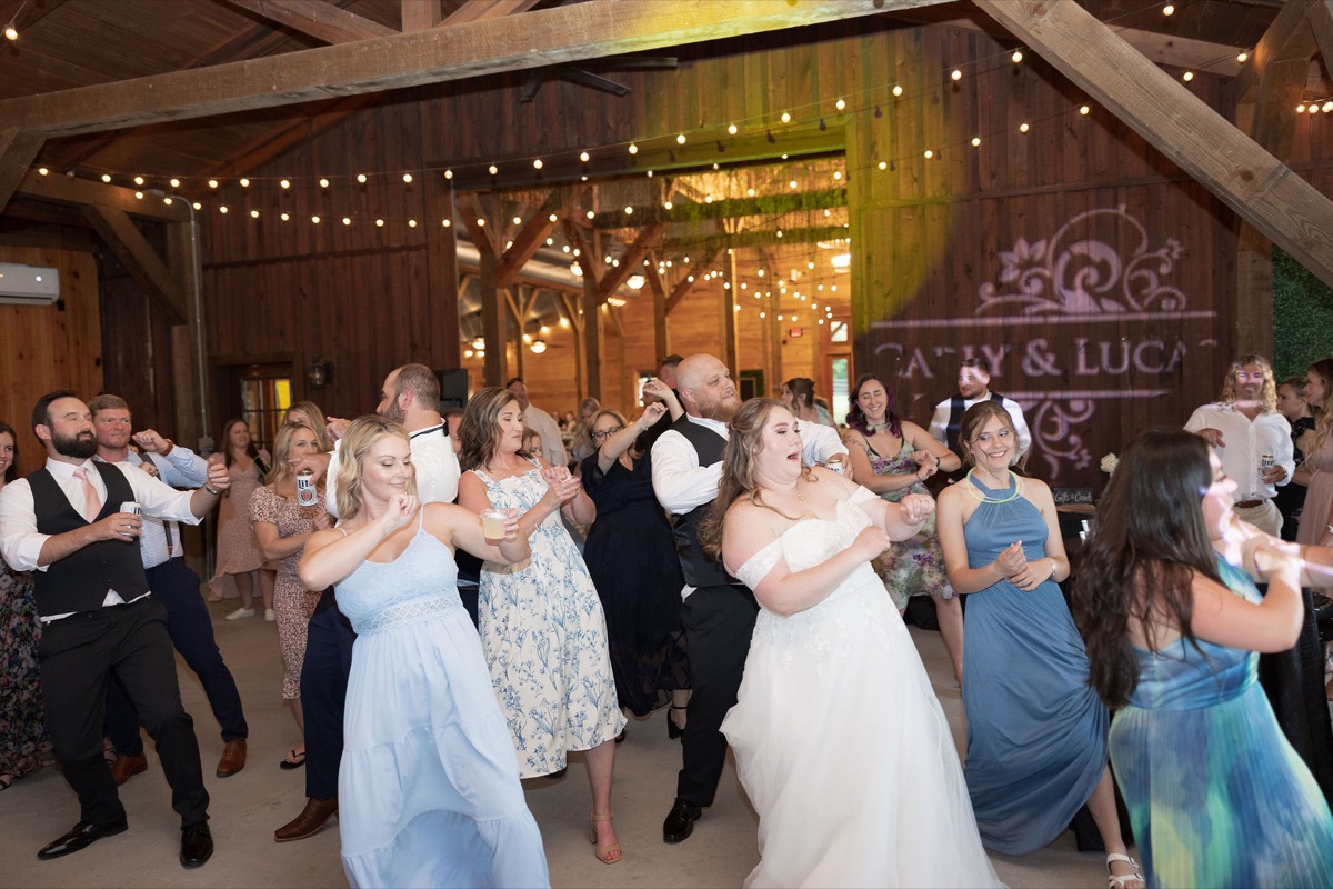 Carly dances with guests under string lights and a Carly & Lucas projection at Covey Creek indoor reception