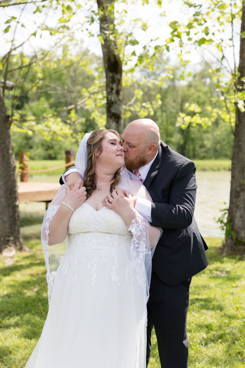 Lucas kisses Carly's cheek in a grassy portrait by the Pond dock at Covey Creek for Carly & Lucas