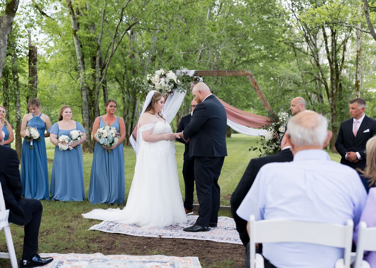 Lucas places a ring on Carly's finger under a wooden arbor at their Tunnel of Love ceremony at Covey Creek