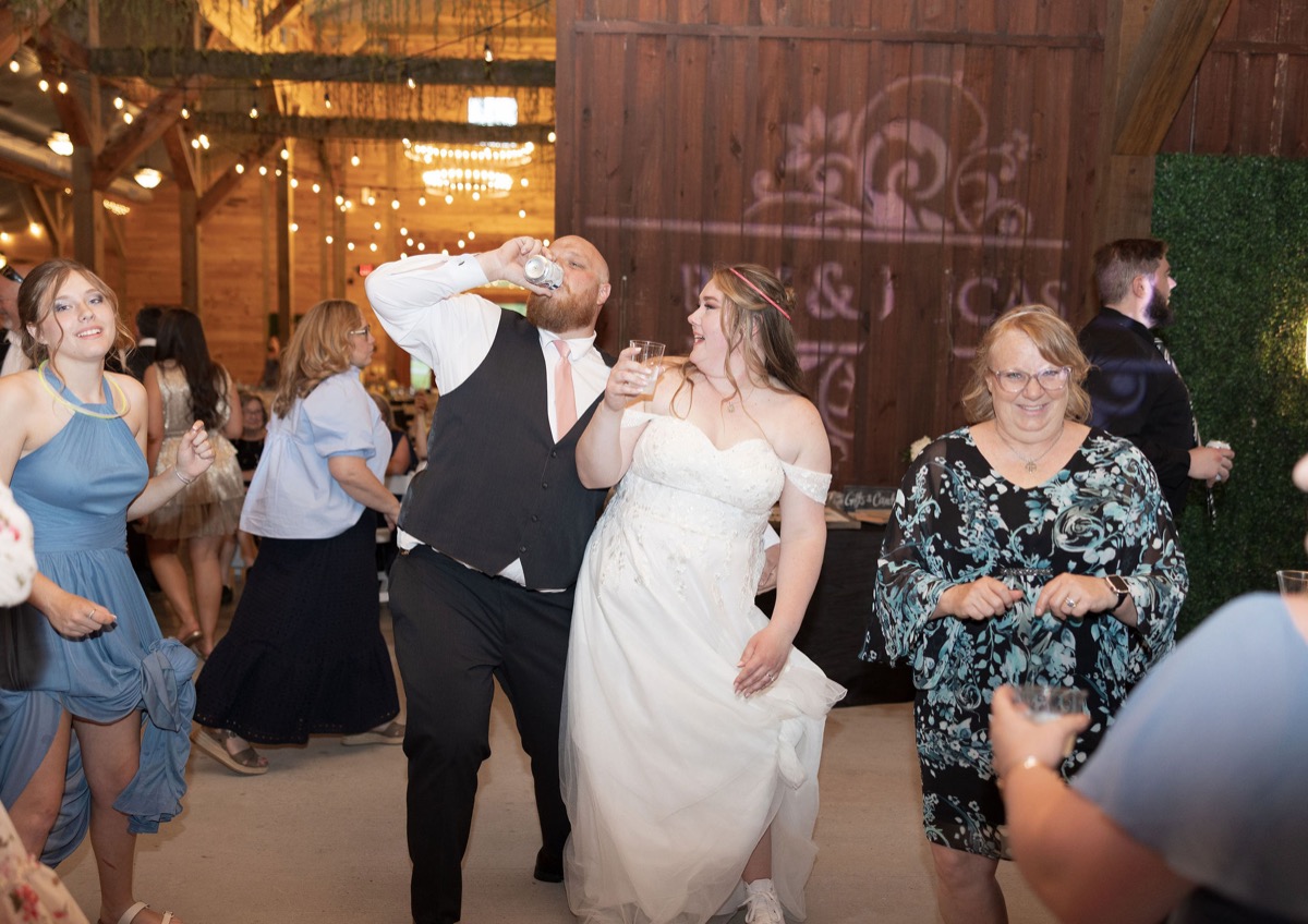 Carly & Lucas laugh on the dance floor with guests at their Covey Creek indoor reception under string lights