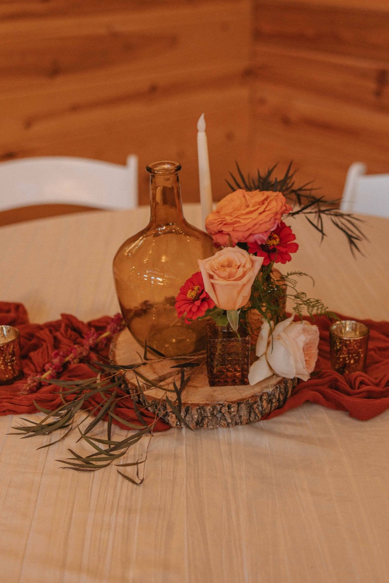 Claire & Jacob reception centerpiece with amber glass, pink roses, and taper on wood slice at Covey Creek