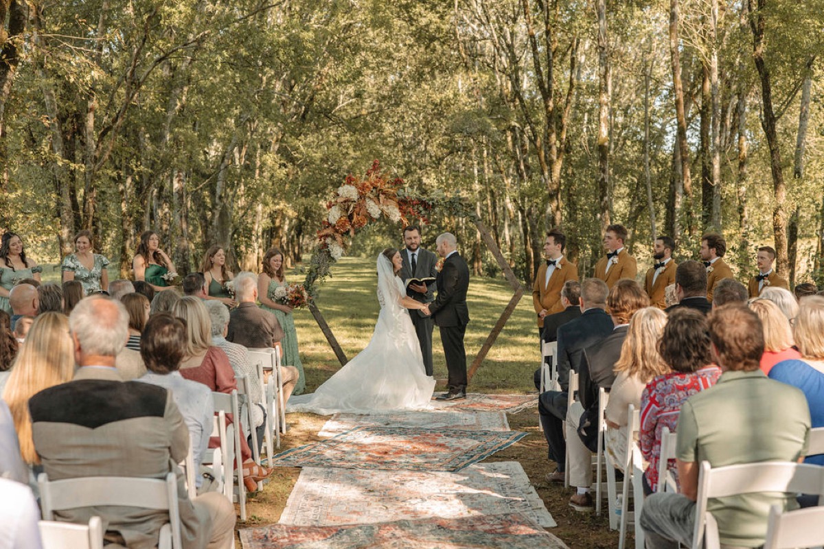 Claire & Jacob exchange vows under a floral hexagon arch with guests seated at Covey Creek