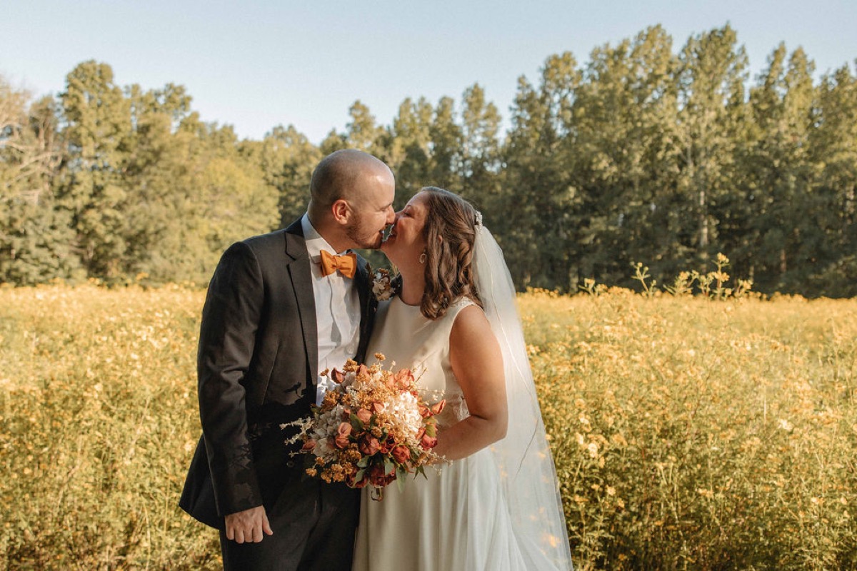 Claire & Jacob lean in for a kiss amid tall yellow wildflowers under blue sky at Covey Creek