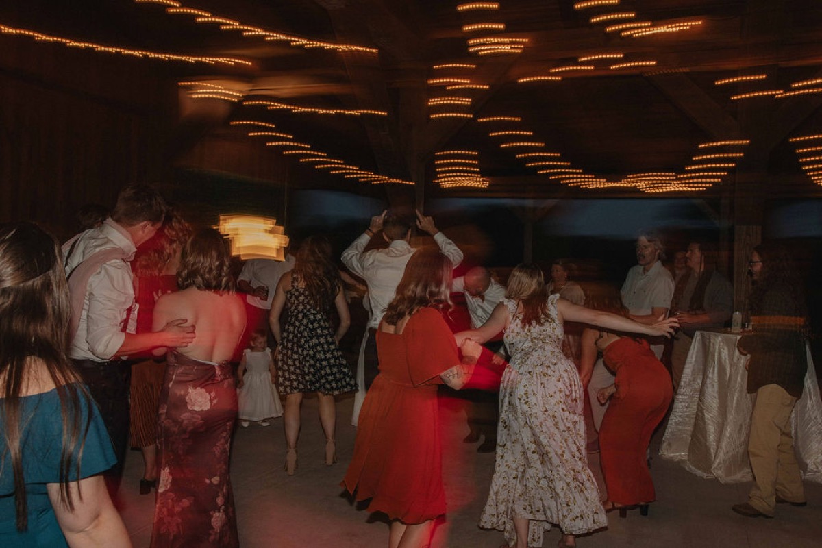 Guests dance under string lights on the barn floor at Claire & Jacob's Covey Creek reception