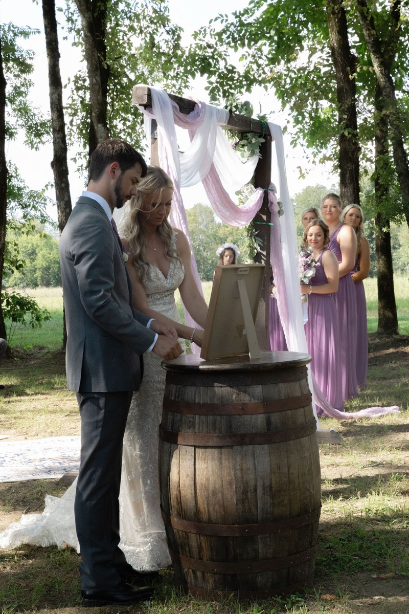 Courtney & Brett sign at a whiskey barrel before their fabric-draped arbor ceremony at Covey Creek