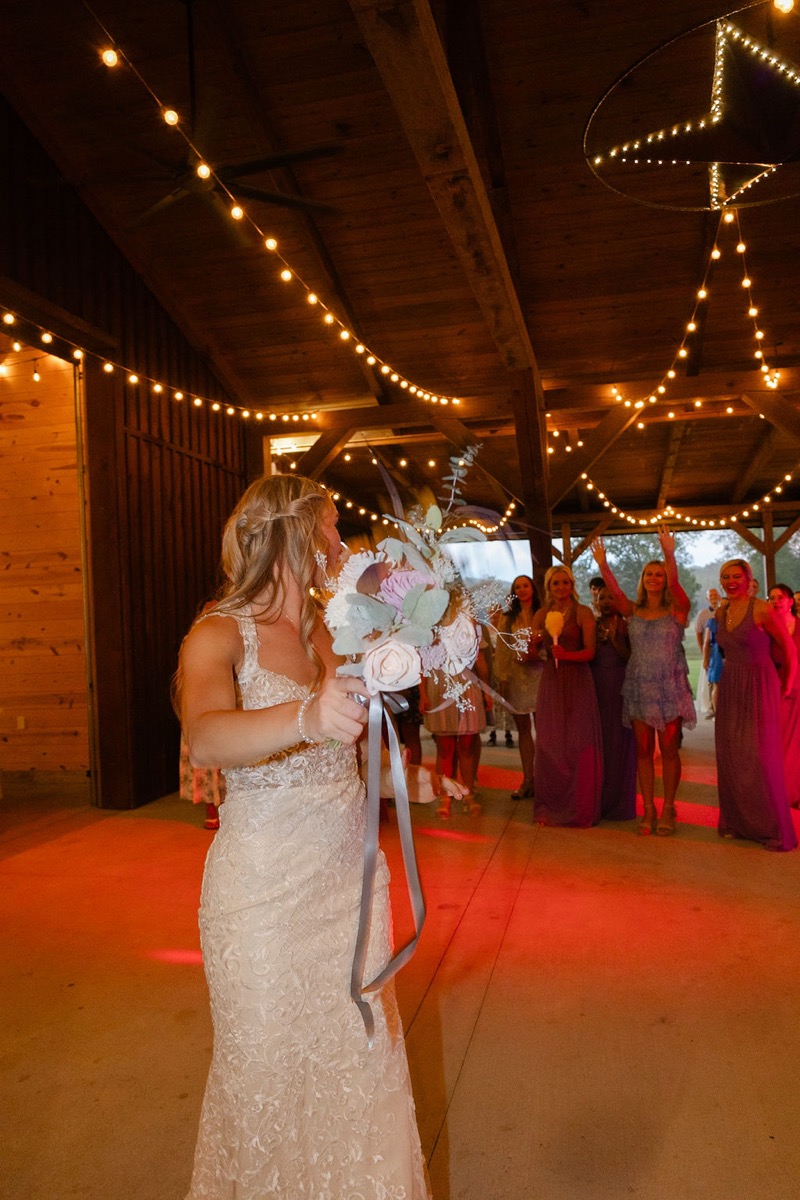 Courtney & Brett: bride tosses her bouquet to cheering guests under string lights at Covey Creek