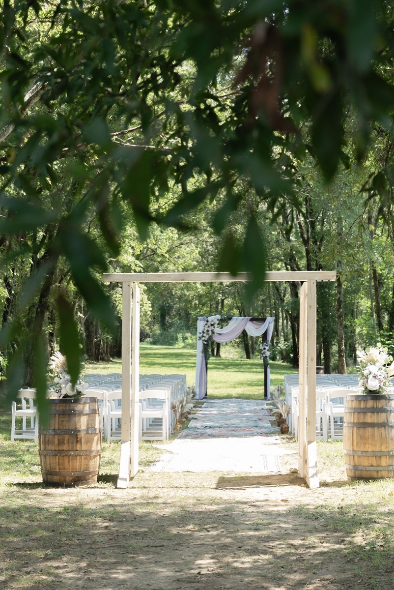 Courtney & Brett outdoor ceremony at Covey Creek with rug aisle, white chairs, and fabric-draped wooden arbor