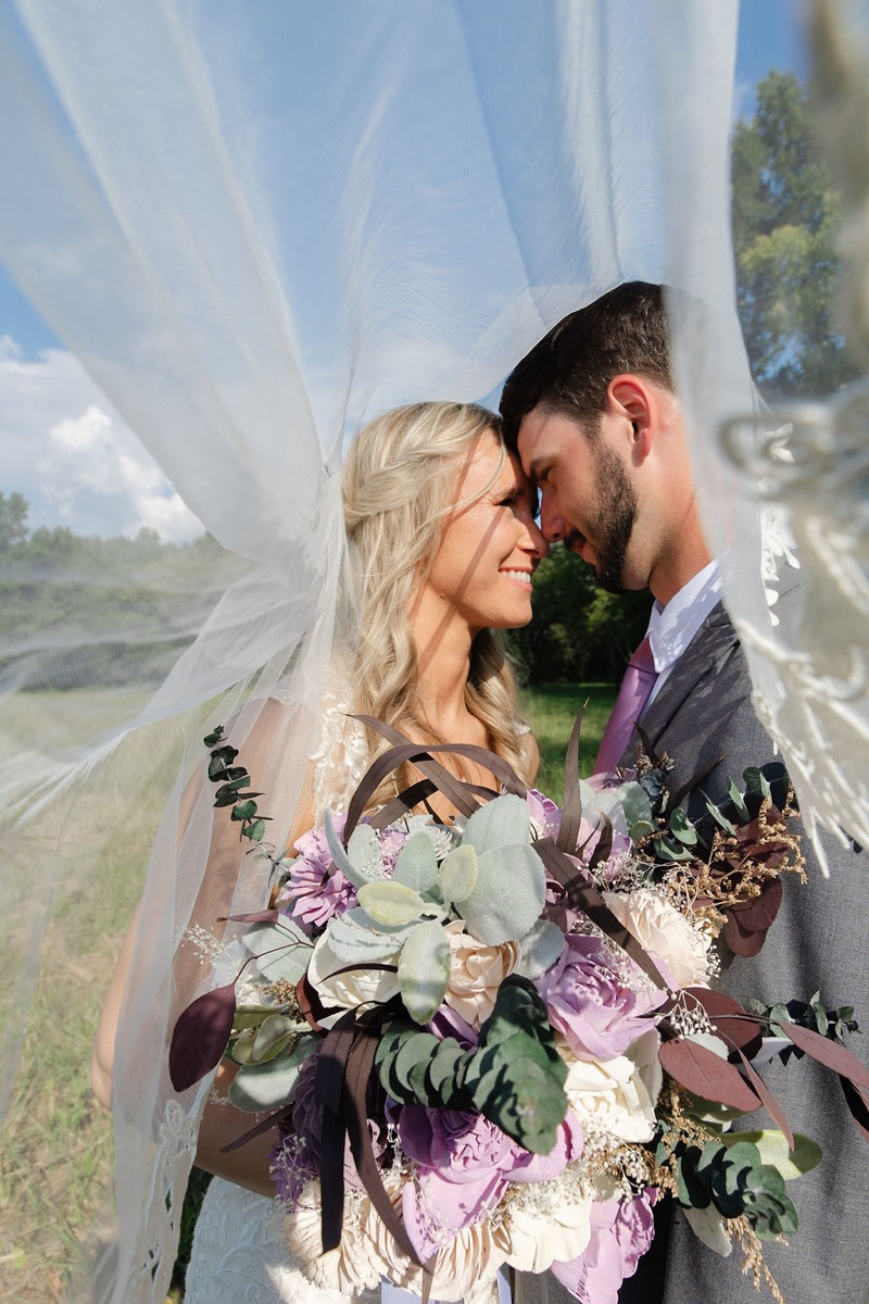 Courtney & Brett smile forehead-to-forehead under her veil with a purple bouquet at Covey Creek