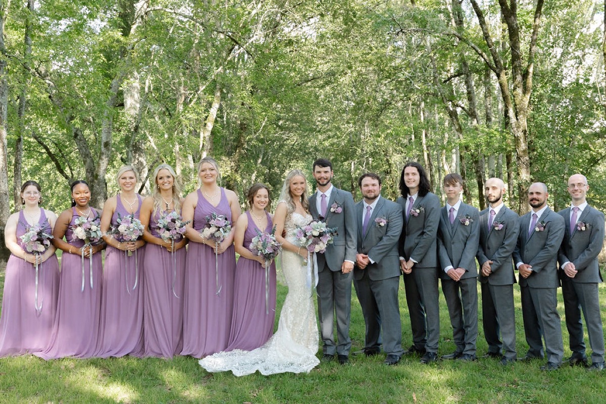 Courtney & Brett wedding party in lavender and grey suits lined up under the trees at Covey Creek