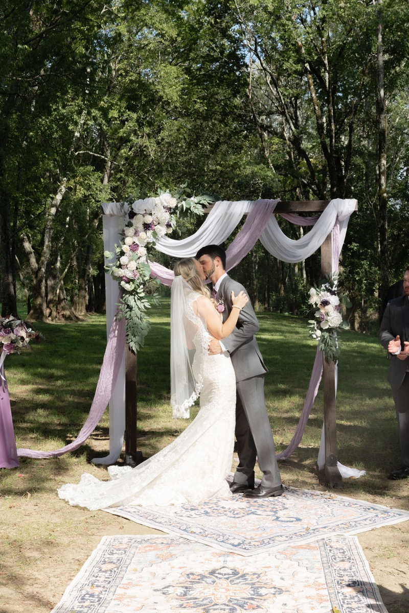 Courtney & Brett share a first kiss under a floral wooden arbor on patterned rugs at Covey Creek