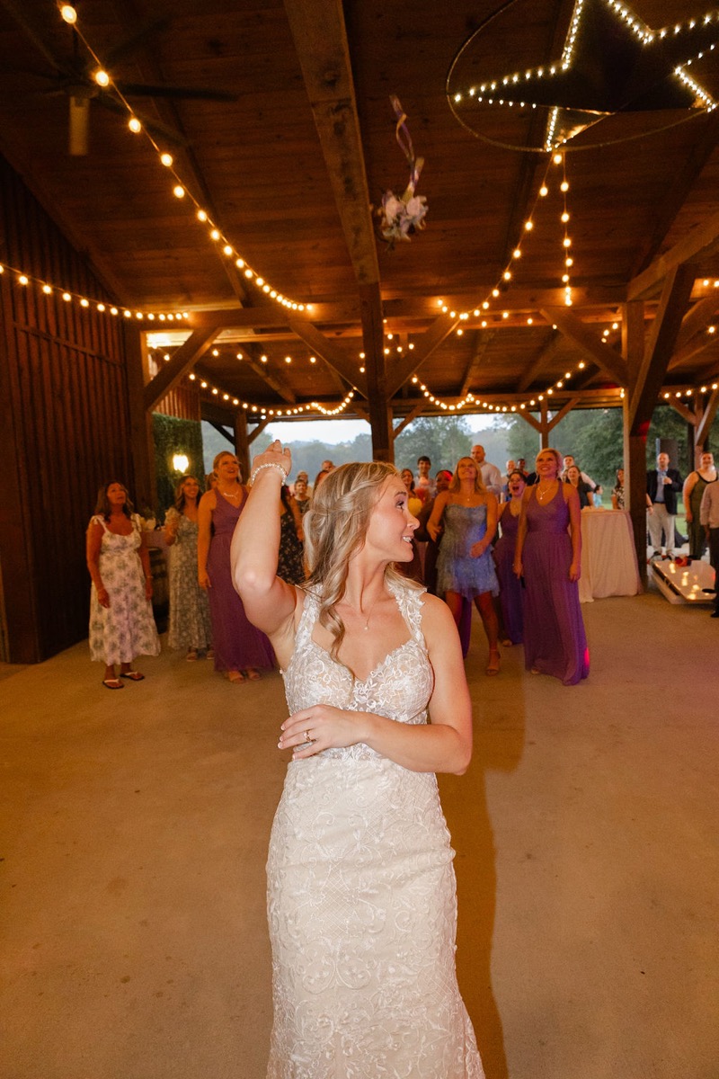Courtney & Brett: bride throws her bouquet under the lit star and bistro lights at Covey Creek