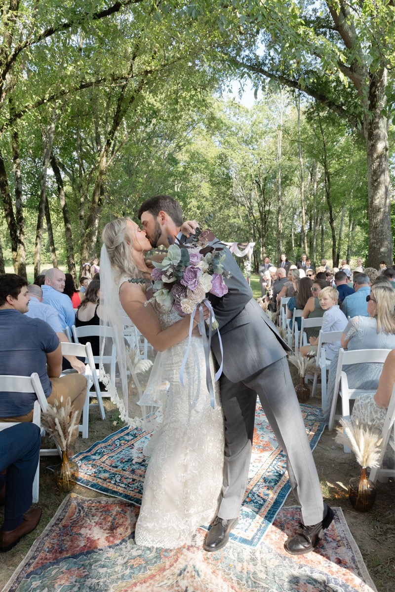 Courtney & Brett kiss mid-aisle on overlapping rugs as guests watch their Covey Creek outdoor ceremony
