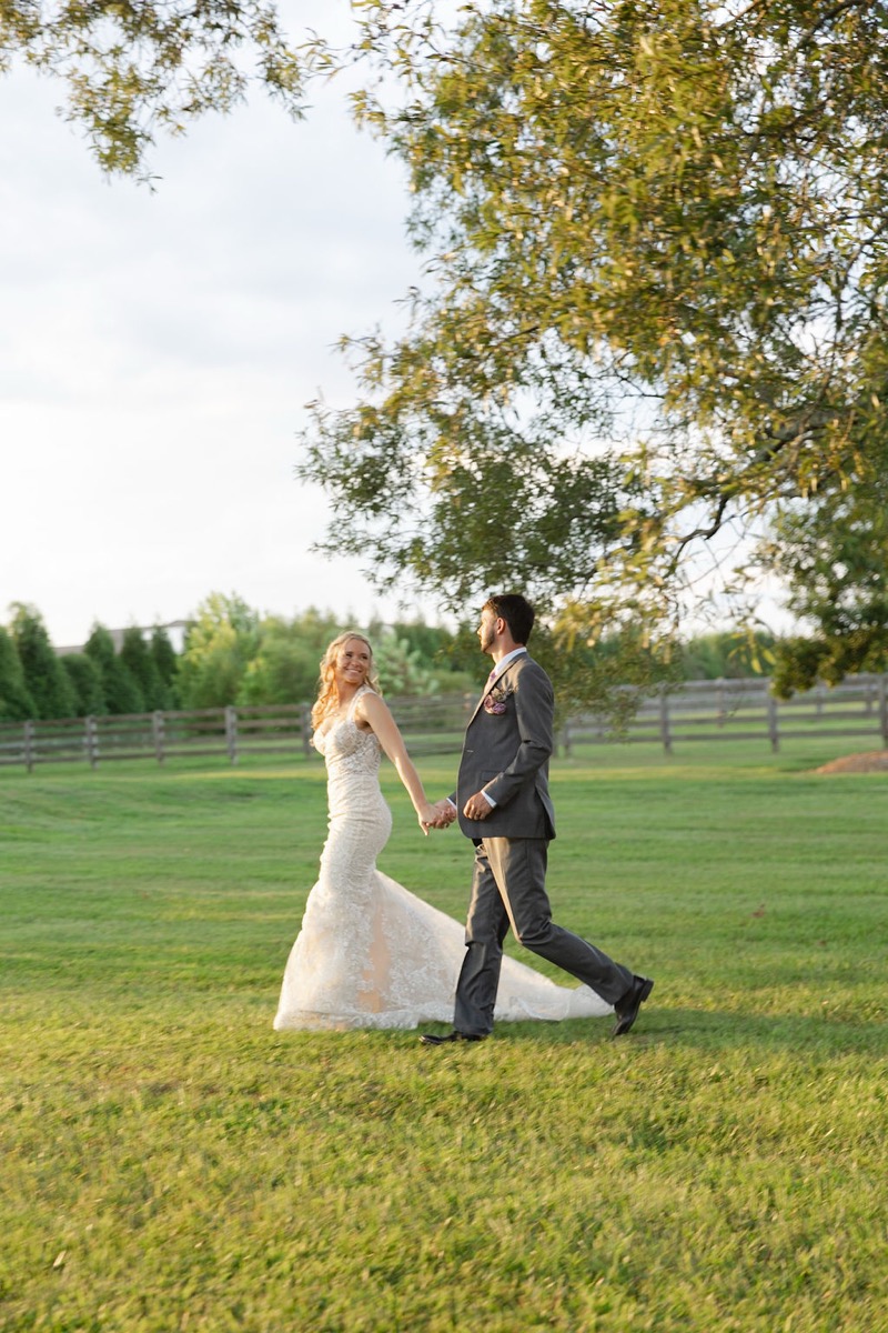 Courtney & Brett walk hand-in-hand across a fenced meadow at golden hour on their Covey Creek wedding day
