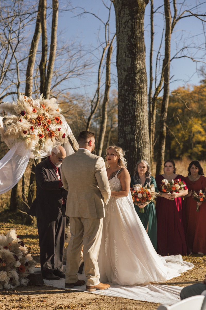 Danika & Troy face each other at the altar with bridesmaids in autumn jewel tones at Covey Creek