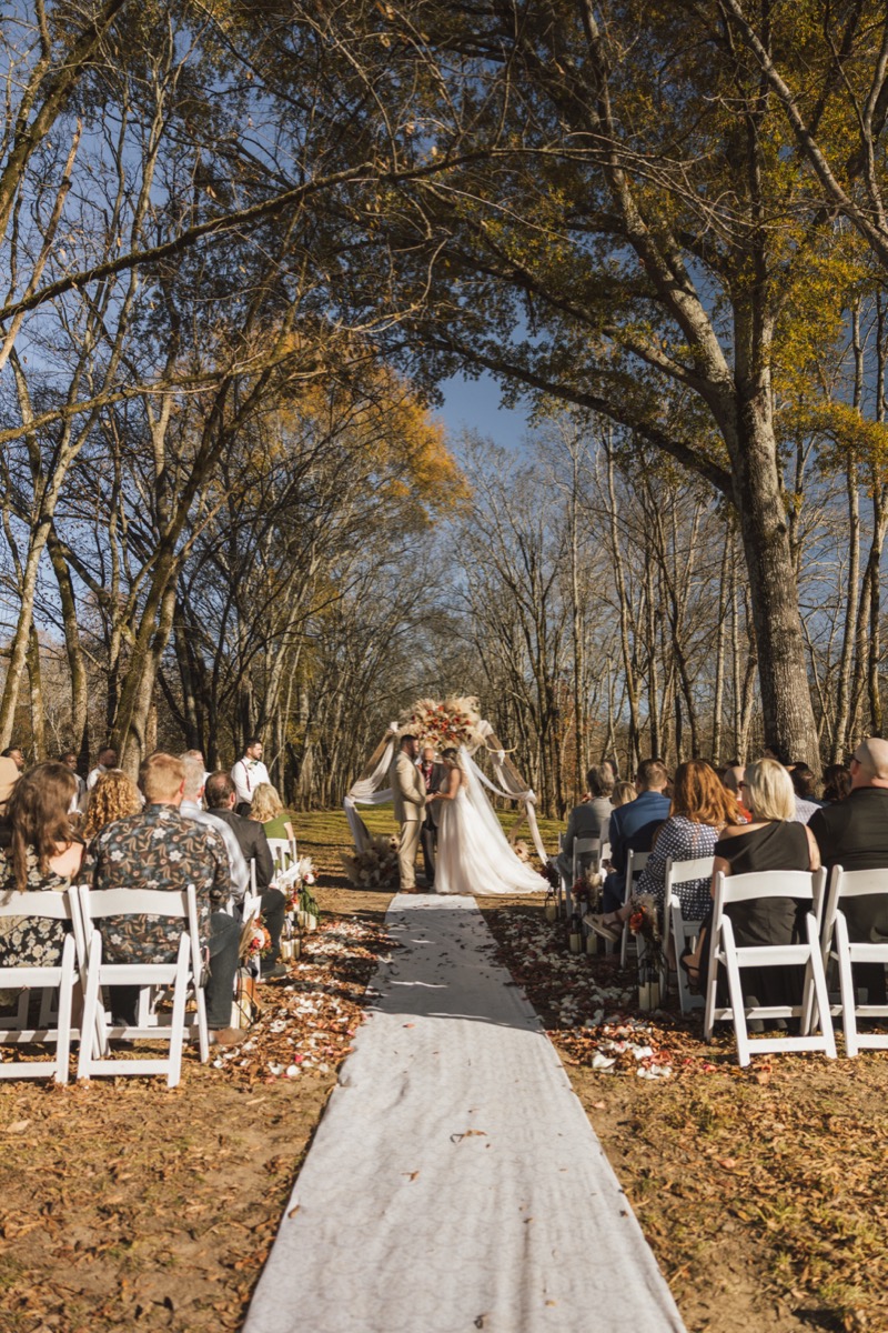 Danika & Troy exchange vows under a pampas-draped wood arch before seated guests at Covey Creek