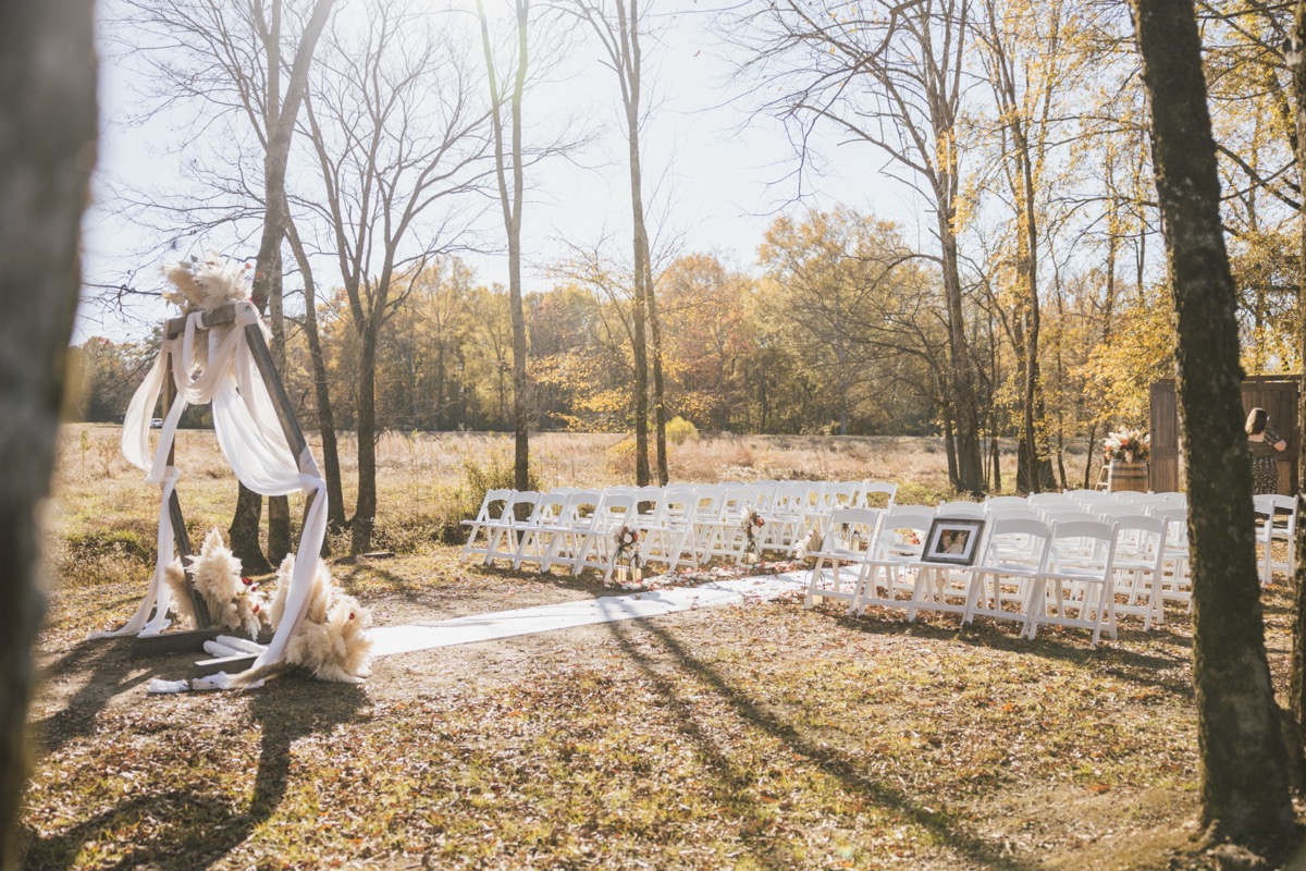 Sunlit hex wood arch with white fabric faces empty chairs for Danika & Troy's ceremony at Covey Creek