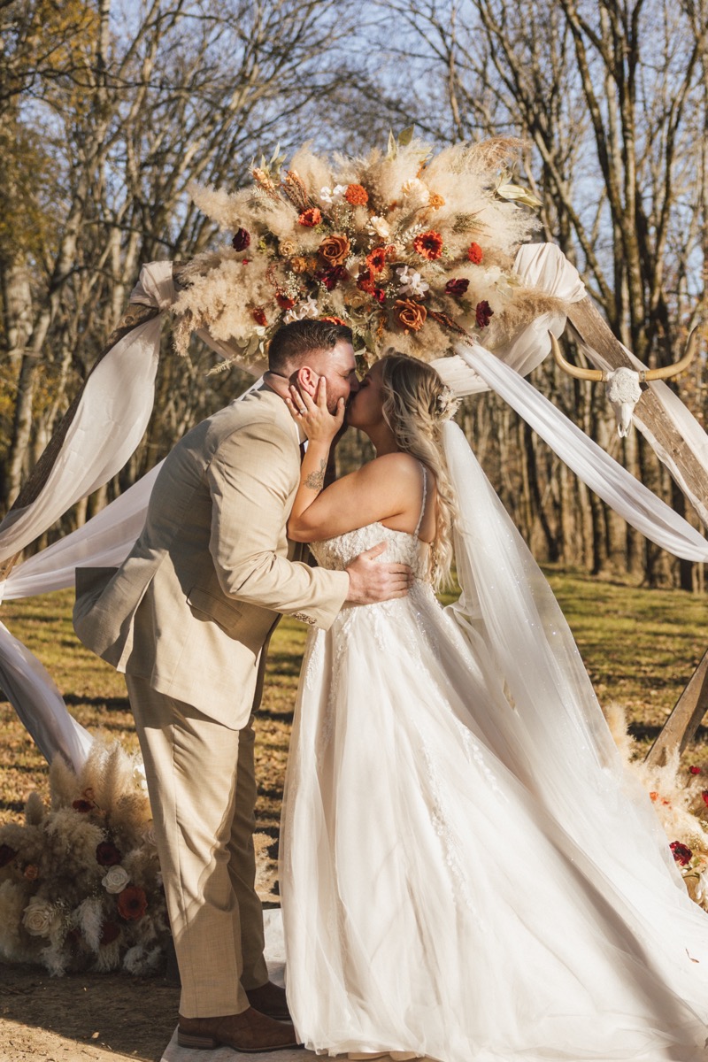 Danika & Troy share a first kiss under their pampas and steer-skull wood arch at Covey Creek