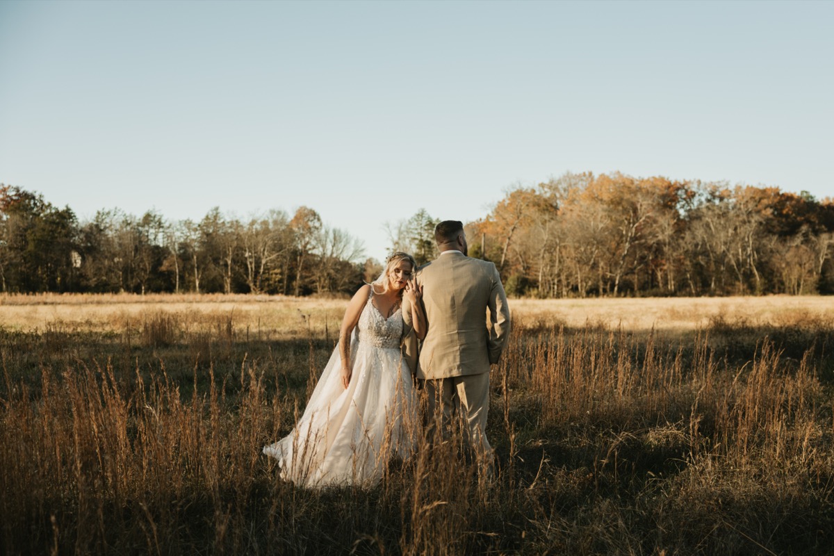 Danika & Troy stand in a tall golden grass field as she leans on his shoulder at Covey Creek