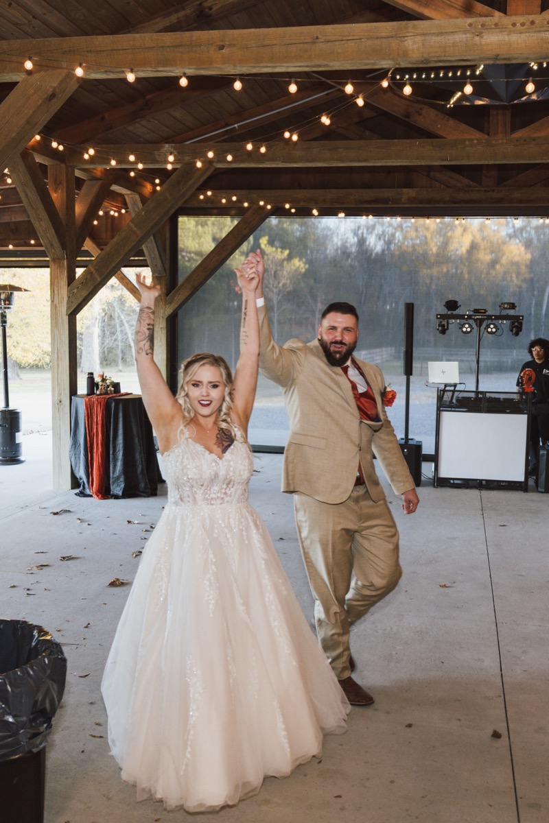 Danika & Troy cheer hand-in-hand under Edison string lights in the pavilion at Covey Creek