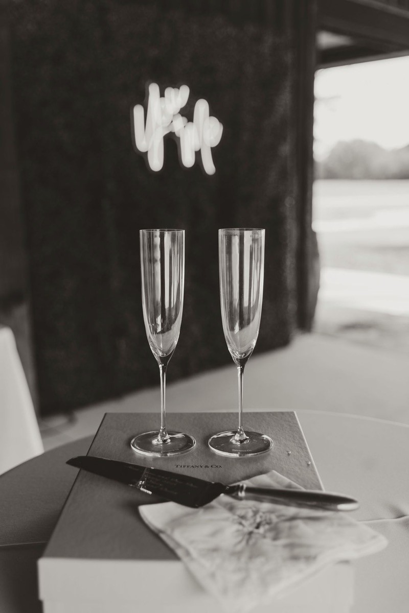 Champagne flutes and silver cake server for Elizabeth & Ashton at Covey Creek beside a Tiffany box and neon sign
