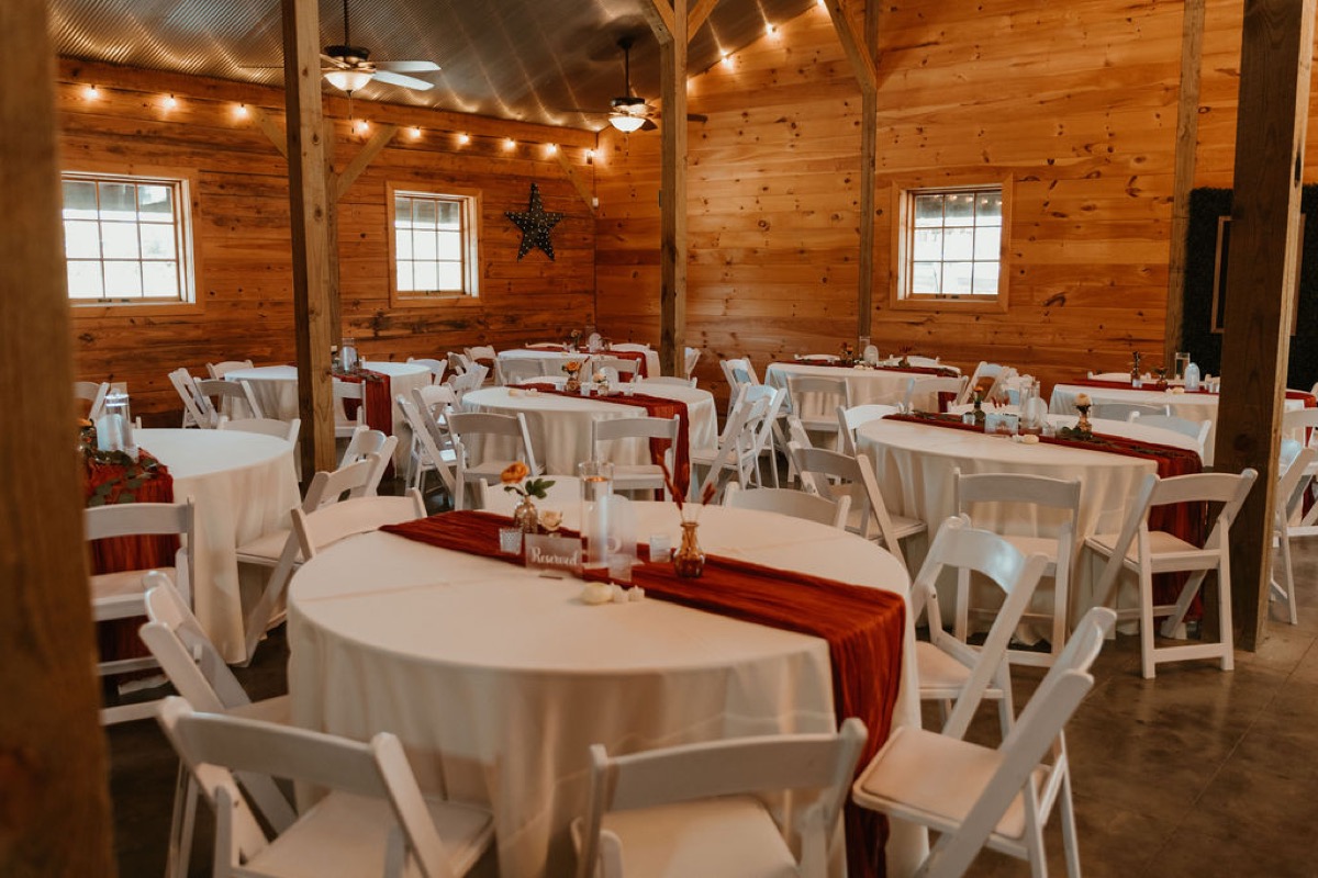 Round guest tables for Elizabeth & Ashton at Covey Creek with rust runners, orange florals, and white chairs