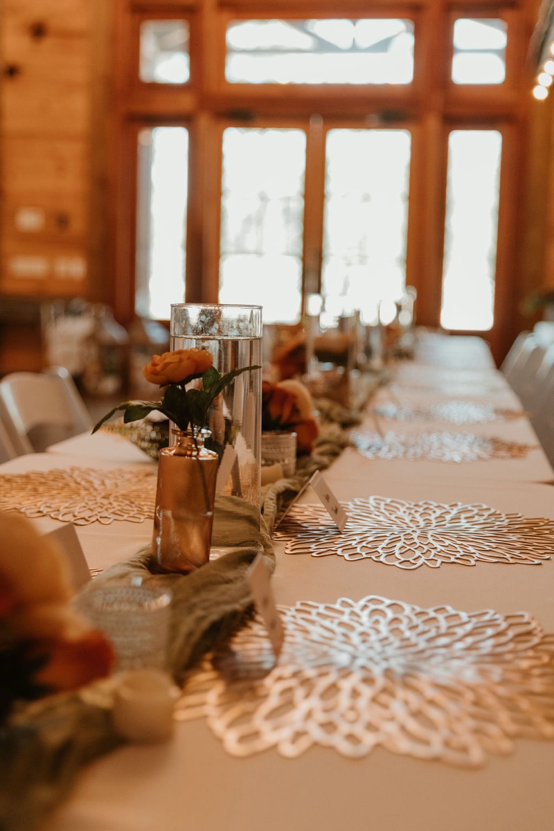 Close-up of Elizabeth & Ashton’s Covey Creek table with copper bud vase, sage runner, and gold filigree placemats