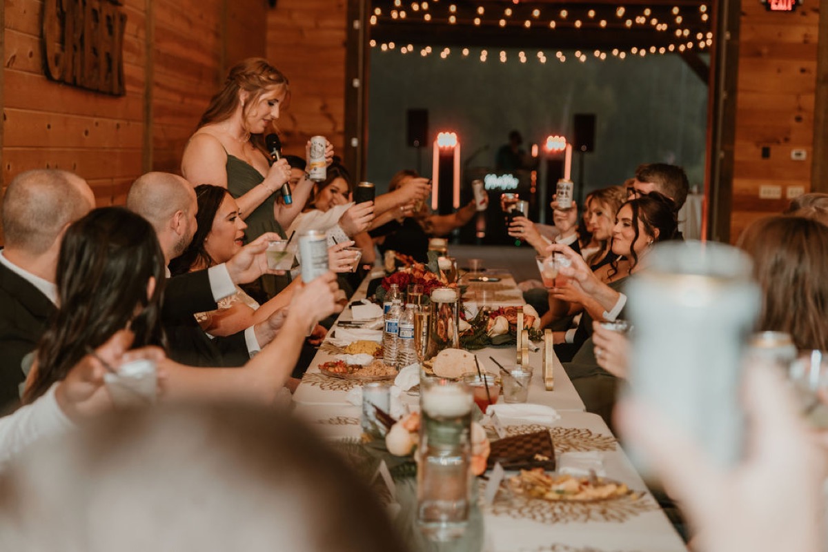 Wedding party toasts as a bridesmaid speaks for Elizabeth & Ashton along Covey Creek’s long reception table