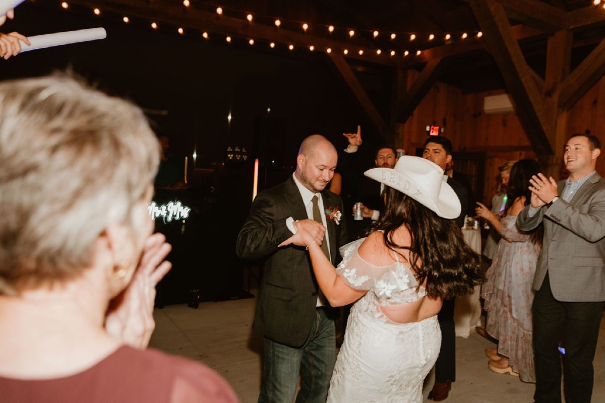 Elizabeth in a Bride cowboy hat dances with Ashton under Covey Creek’s string lights and Mr & Mrs neon