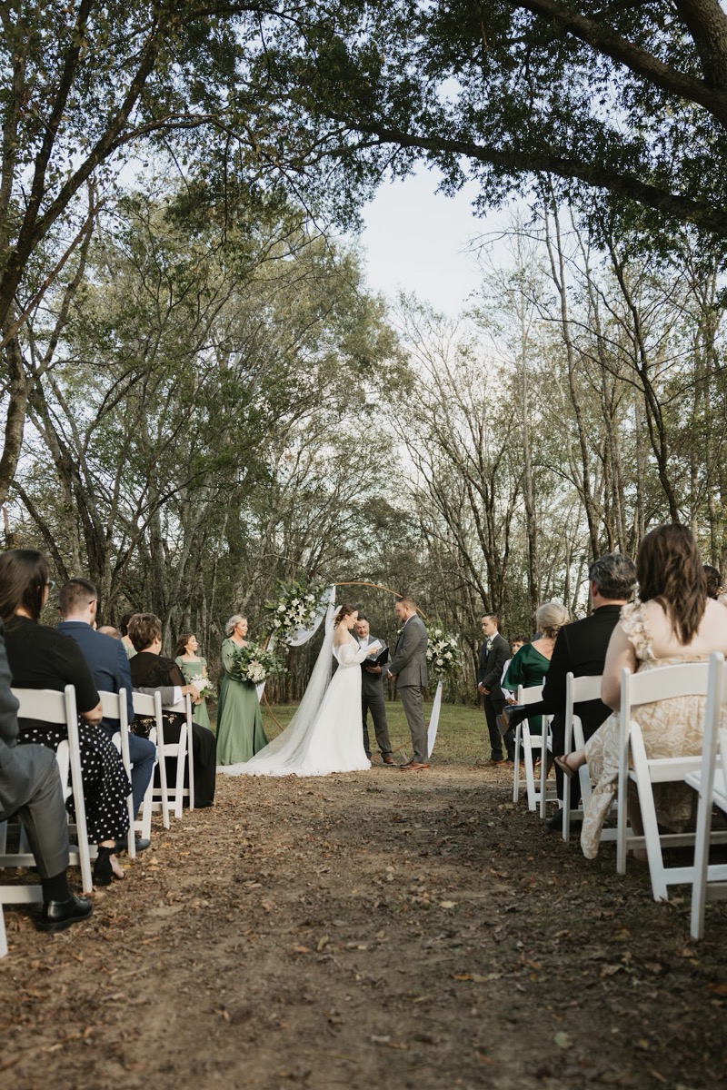 Emily & Bryan exchange vows under a floral circular arch beneath the Tunnel of Love tree canopy at Covey Creek.