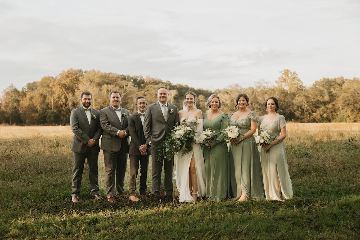 Emily & Bryan stand with their wedding party in sage and grey across a golden field lined with autumn trees at Covey Creek.