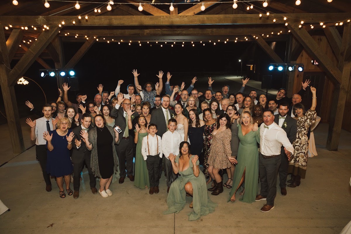 Emily & Bryan celebrate with guests arms raised under warm string lights on the covered Patio at Covey Creek.