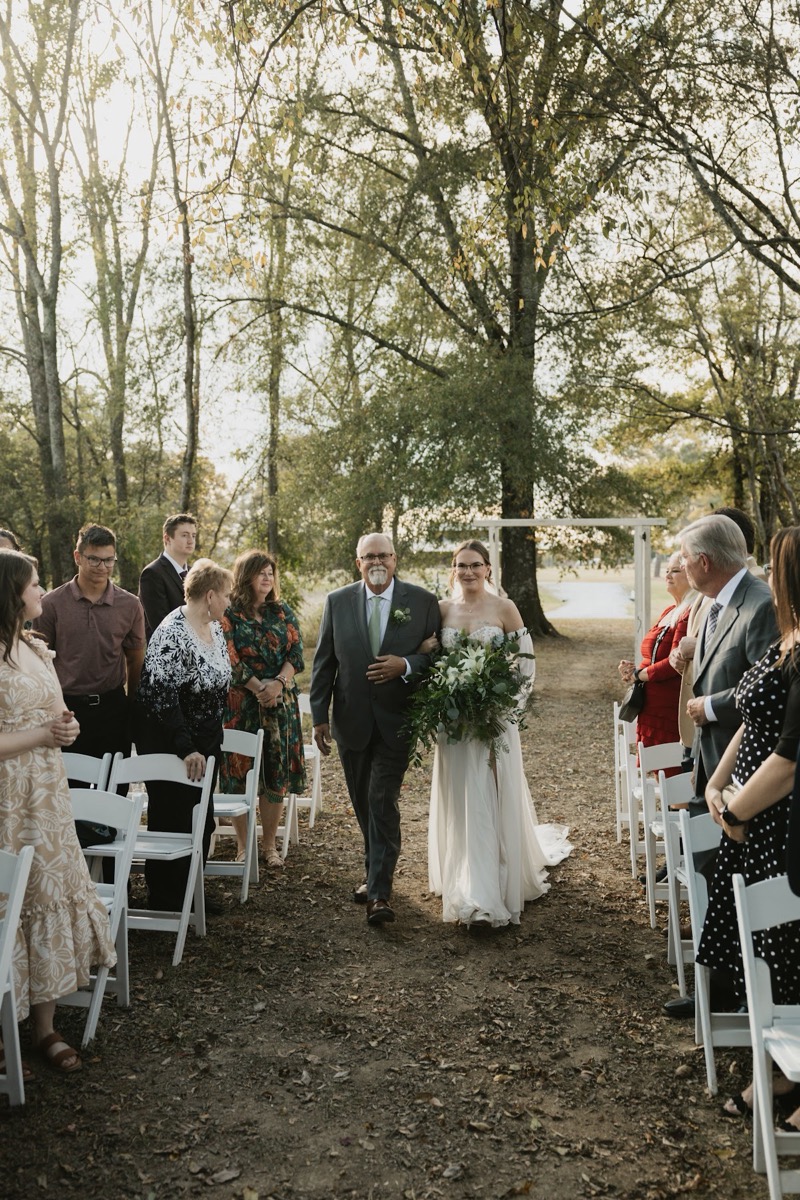 Emily & Bryan's day begins as Emily walks a leafy wooded aisle arm-in-arm with her father at Covey Creek.