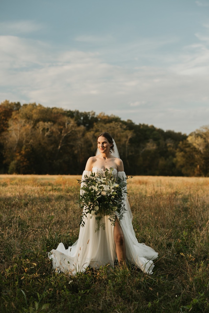Emily holds a cascading lily bouquet in an open golden field during Emily & Bryan's wedding portraits at Covey Creek.