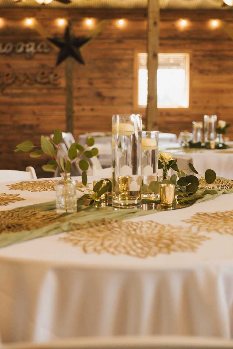 Gold filigree placemats and floating candles dress Emily & Bryan's indoor reception tables under string lights at Covey Creek.