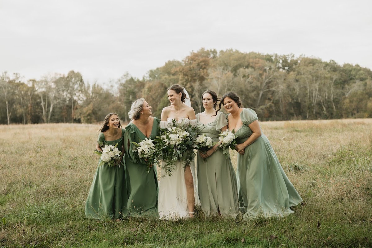 Emily laughs with sage-dressed bridesmaids holding white bouquets in a golden field during Emily & Bryan's day at Covey Creek.