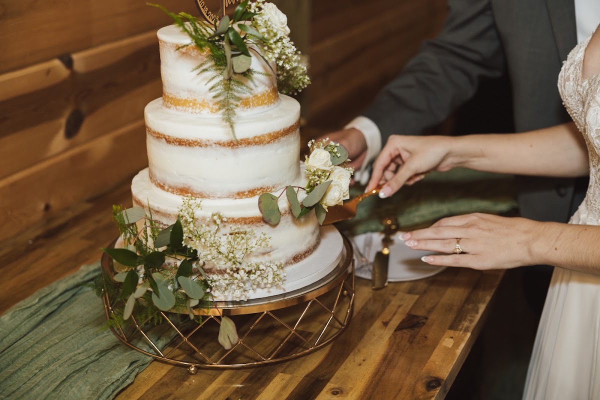 Emily & Bryan cut a three-tier naked cake topped with eucalyptus and white roses at their indoor reception at Covey Creek.