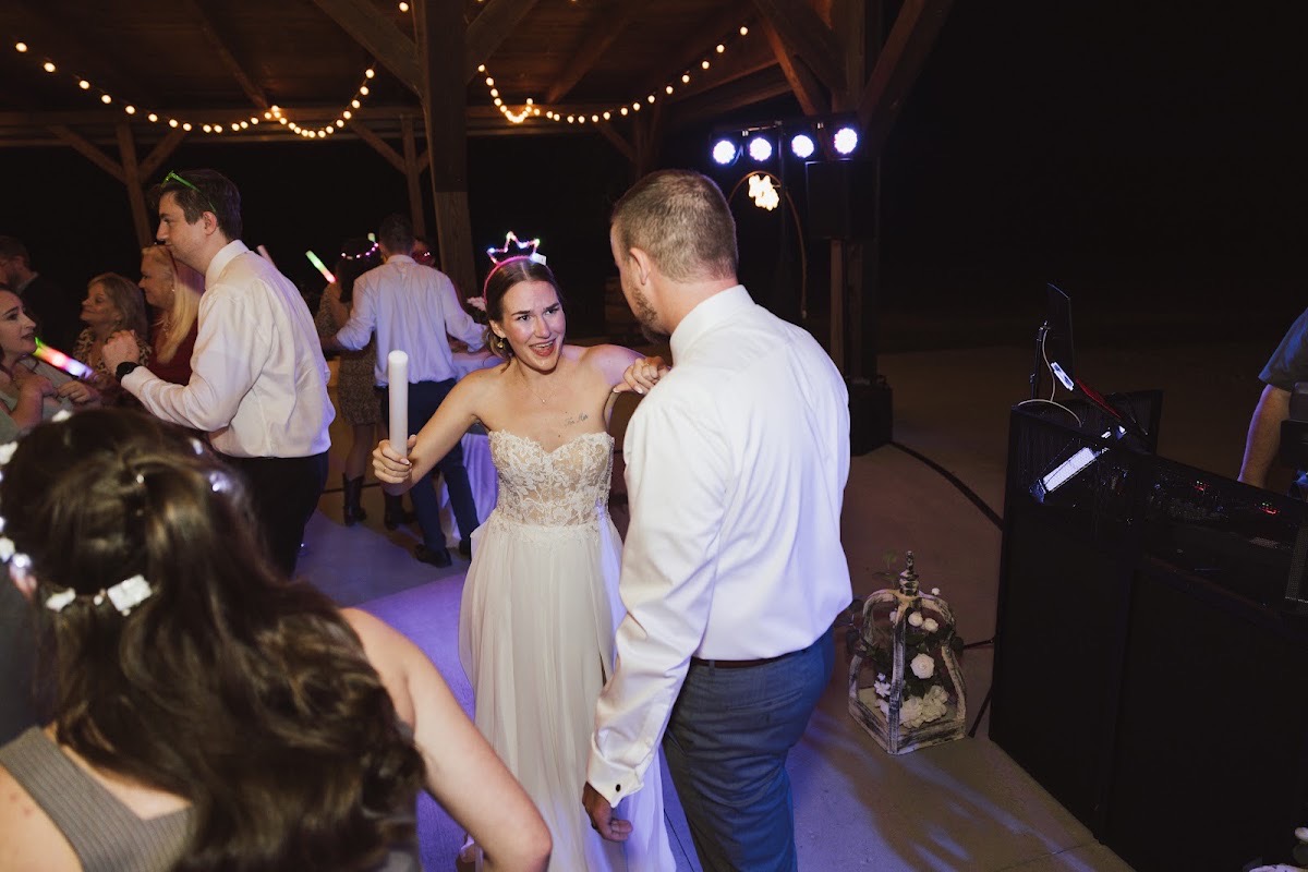 Emily & Bryan dance under Patio string lights as guests wave glow sticks at their Covey Creek reception party.