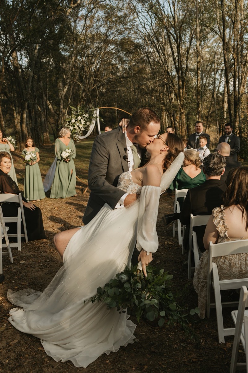 Emily & Bryan share a romantic dip kiss in the leafy aisle before a floral circular arch at Covey Creek.