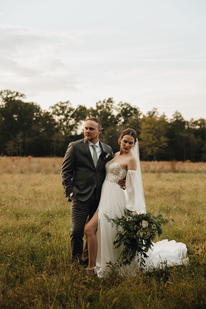 Emily & Bryan stand in a wide golden field, her lace gown and veil catching soft light beside his grey suit at Covey Creek.