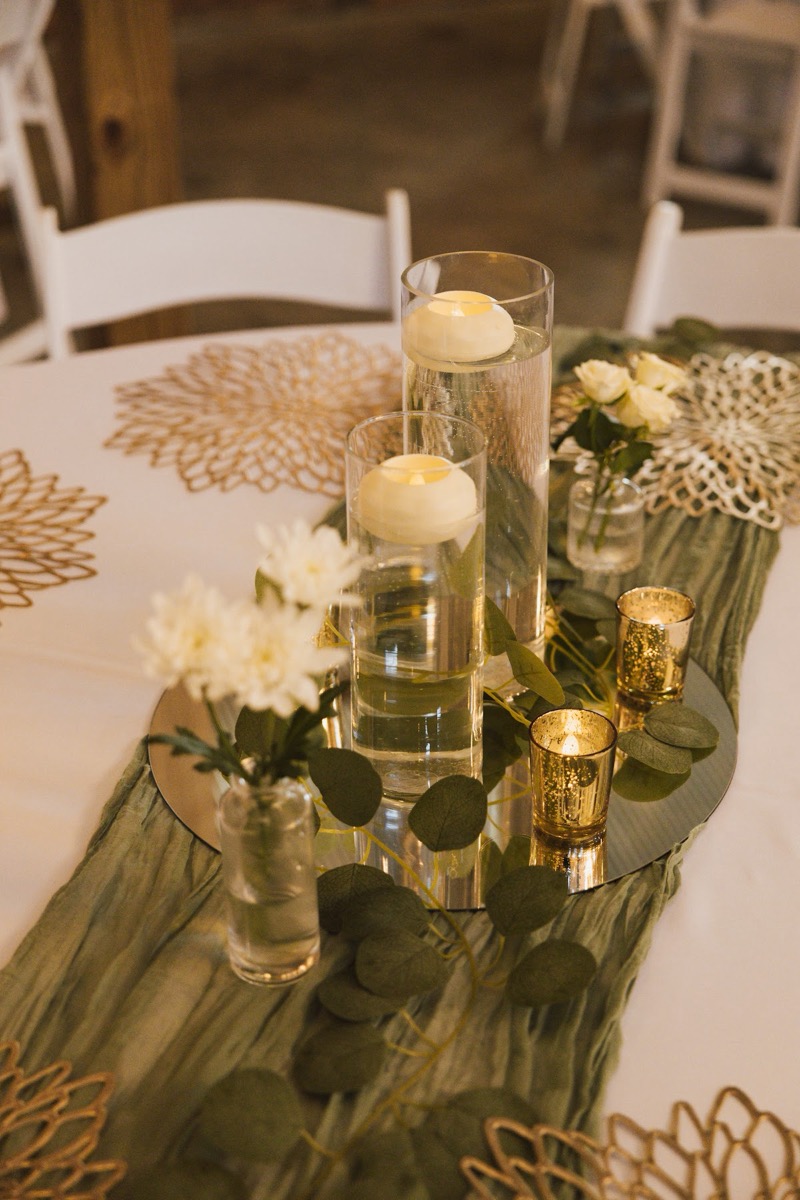 Floating candles, eucalyptus, and gold votives adorn a sage runner on Emily & Bryan's indoor reception table at Covey Creek.